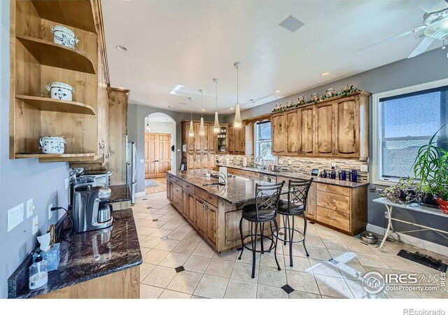 kitchen with ceiling fan, pendant lighting, backsplash, a kitchen bar, and a spacious island