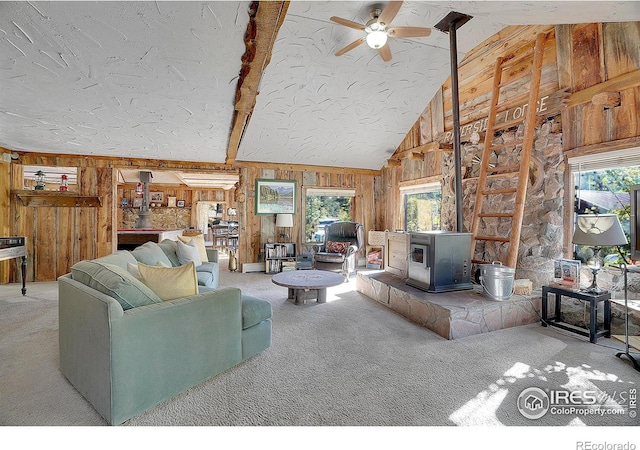 carpeted living room with beamed ceiling, high vaulted ceiling, a wood stove, and ceiling fan