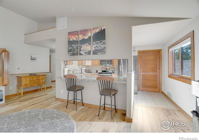 kitchen featuring lofted ceiling, light stone countertops, appliances with stainless steel finishes, a kitchen bar, and kitchen peninsula