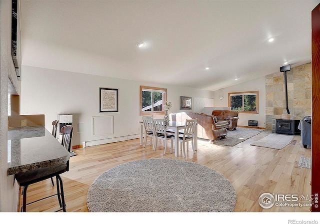 living room featuring vaulted ceiling, a baseboard radiator, a wood stove, and a wealth of natural light