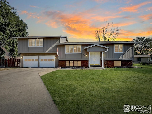 bi-level home featuring fence, concrete driveway, a lawn, brick siding, and a garage
