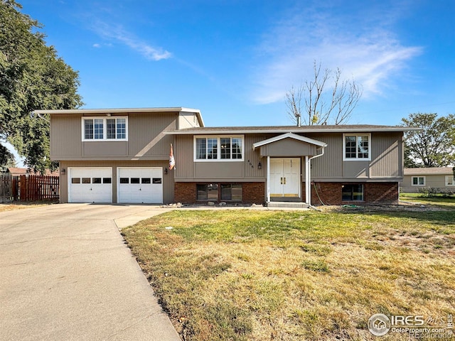 split foyer home featuring a front lawn, driveway, an attached garage, fence, and brick siding