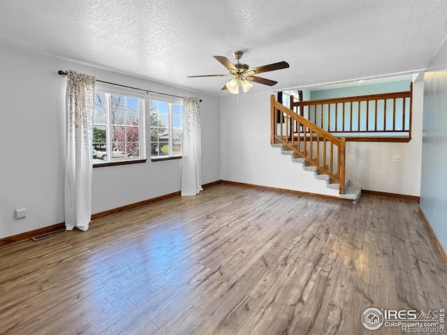 unfurnished living room with a textured ceiling, visible vents, a ceiling fan, wood finished floors, and stairway