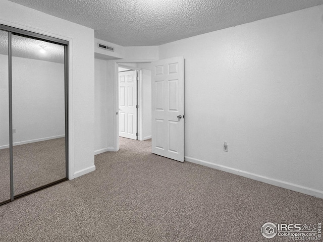 unfurnished bedroom with a textured ceiling, a closet, carpet, baseboards, and visible vents