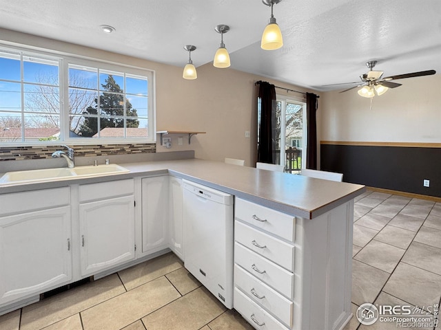 kitchen with white dishwasher, a sink, light tile patterned floors, a peninsula, and white cabinetry