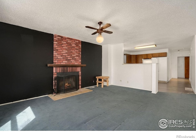 unfurnished living room with a brick fireplace, ceiling fan, carpet floors, and a textured ceiling