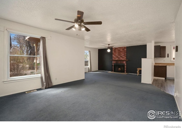 unfurnished living room with a fireplace, ceiling fan, dark carpet, and a textured ceiling