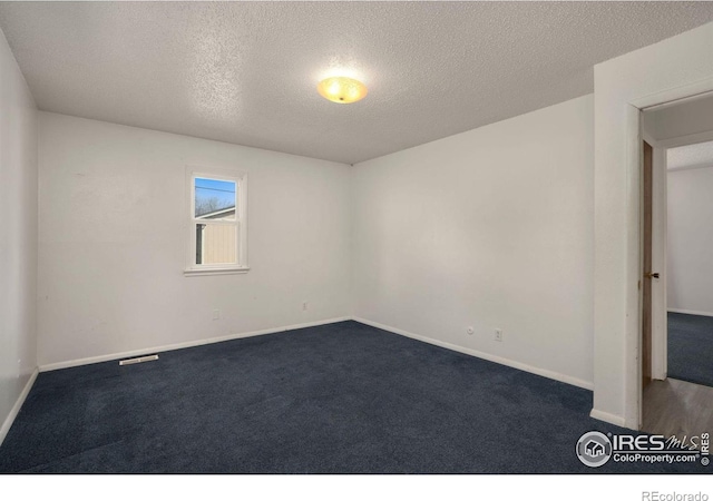 spare room with dark carpet and a textured ceiling