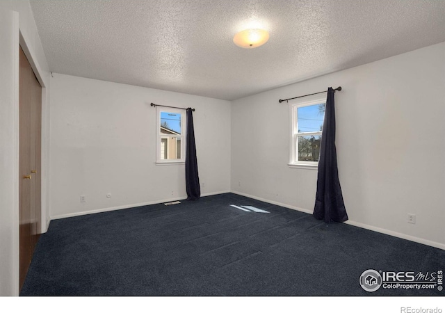 spare room featuring dark carpet and a textured ceiling