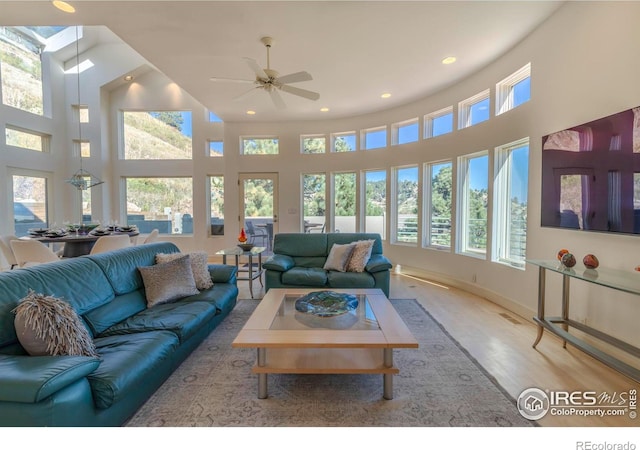 living room with ceiling fan, a skylight, light hardwood / wood-style flooring, and a towering ceiling