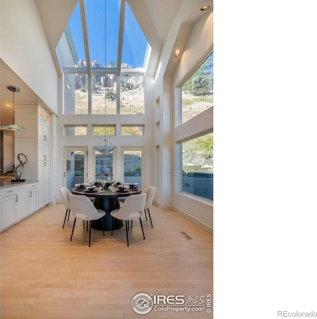 dining area featuring a skylight, light hardwood / wood-style floors, and a high ceiling