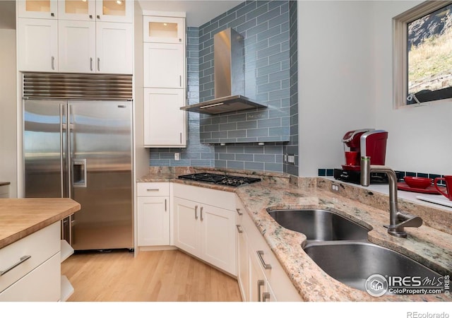 kitchen featuring white cabinets, stainless steel appliances, wall chimney range hood, and light hardwood / wood-style flooring