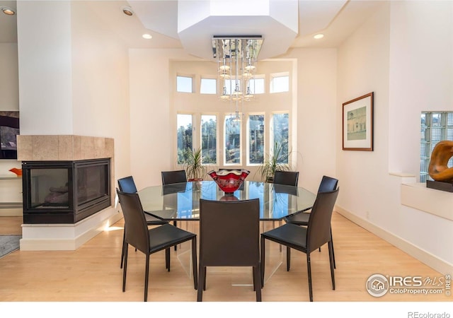 dining room with a multi sided fireplace, light wood-type flooring, a healthy amount of sunlight, and an inviting chandelier