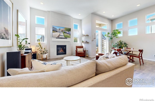 living room featuring light wood-type flooring, a large fireplace, and a healthy amount of sunlight