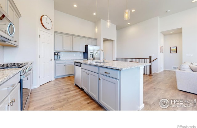 kitchen with gray cabinetry, light wood-type flooring, sink, an island with sink, and appliances with stainless steel finishes