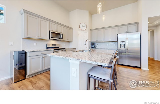 kitchen with light stone counters, stainless steel appliances, sink, and light hardwood / wood-style flooring