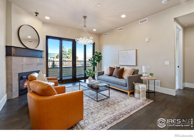 living room with dark wood-type flooring, an inviting chandelier, and a tile fireplace