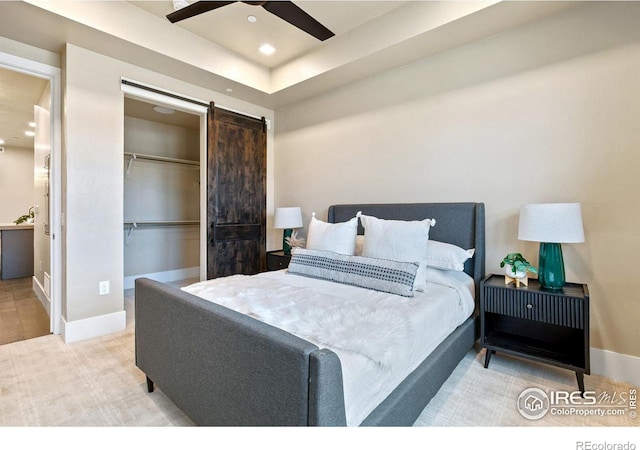 bedroom with ceiling fan, a barn door, a closet, and a tray ceiling