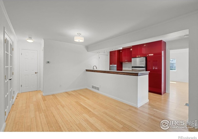 kitchen with light wood-type flooring, stainless steel refrigerator, wall oven, kitchen peninsula, and ornamental molding