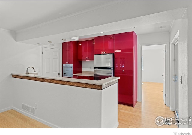 kitchen featuring oven, stainless steel fridge, light hardwood / wood-style floors, kitchen peninsula, and crown molding