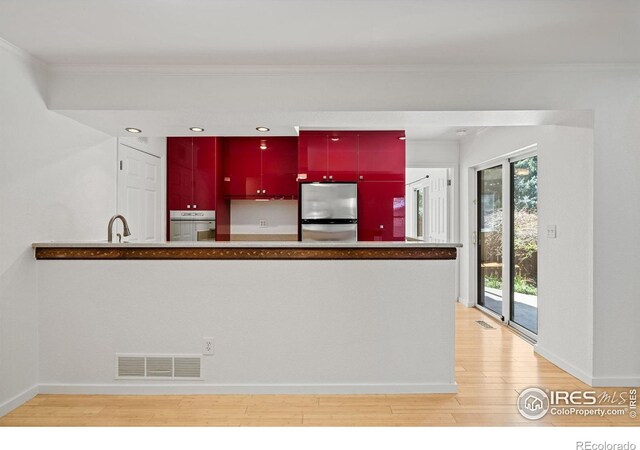 kitchen with ornamental molding, stainless steel appliances, and light hardwood / wood-style flooring