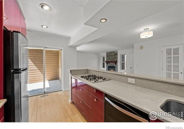 kitchen featuring a stone fireplace, a textured ceiling, stainless steel appliances, and light hardwood / wood-style flooring