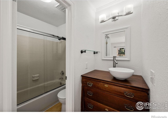 full bathroom featuring vanity, ornamental molding, a textured ceiling, combined bath / shower with glass door, and toilet