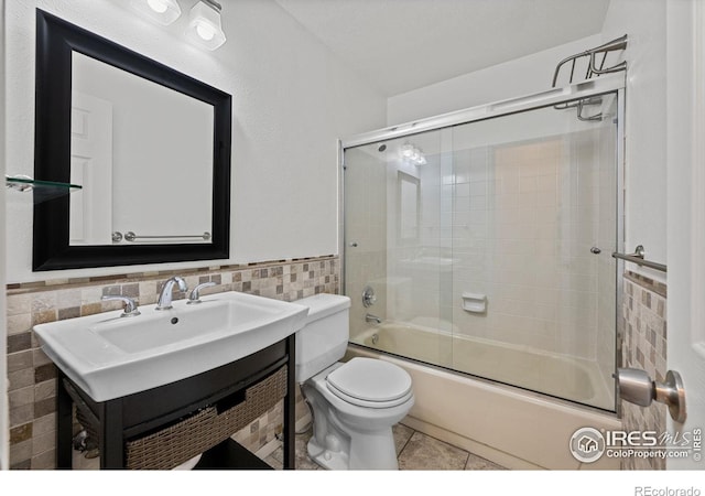 full bathroom featuring tile patterned flooring, combined bath / shower with glass door, toilet, tile walls, and vanity