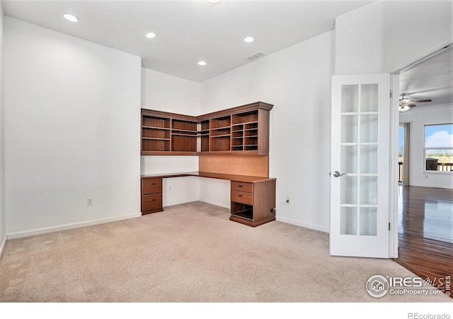 unfurnished office with ceiling fan, light colored carpet, and built in desk