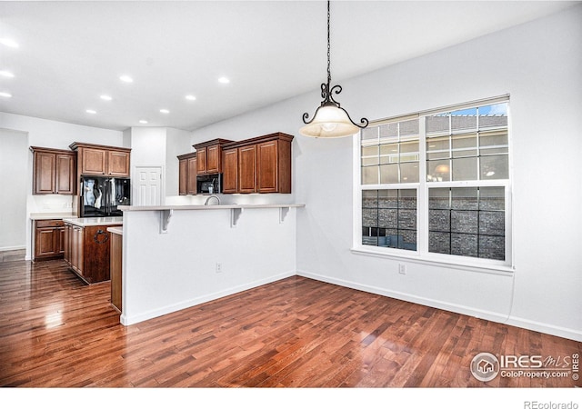 kitchen with a breakfast bar, dark wood-type flooring, hanging light fixtures, and black appliances