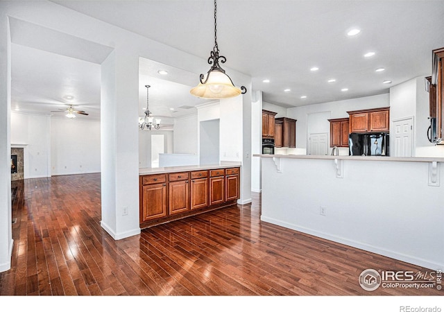 kitchen featuring dark hardwood / wood-style floors, black appliances, kitchen peninsula, a kitchen bar, and hanging light fixtures