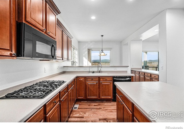 kitchen featuring light wood-type flooring, sink, pendant lighting, and black appliances