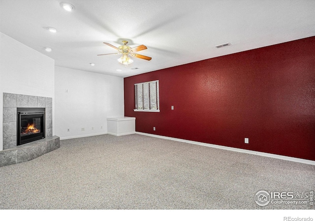 unfurnished living room featuring carpet floors, ceiling fan, and a tiled fireplace