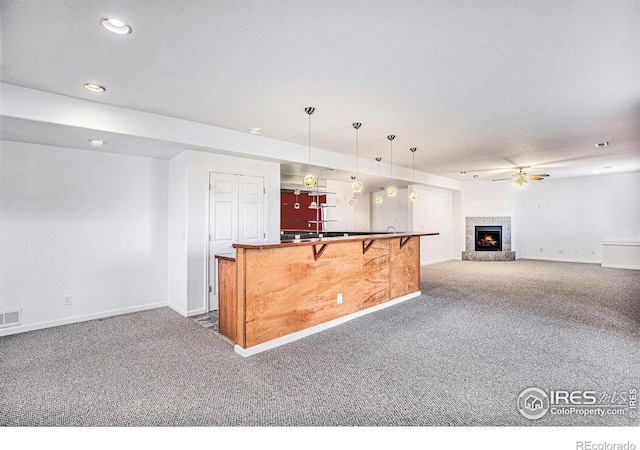 kitchen with decorative light fixtures, a kitchen bar, dark colored carpet, ceiling fan, and a tile fireplace