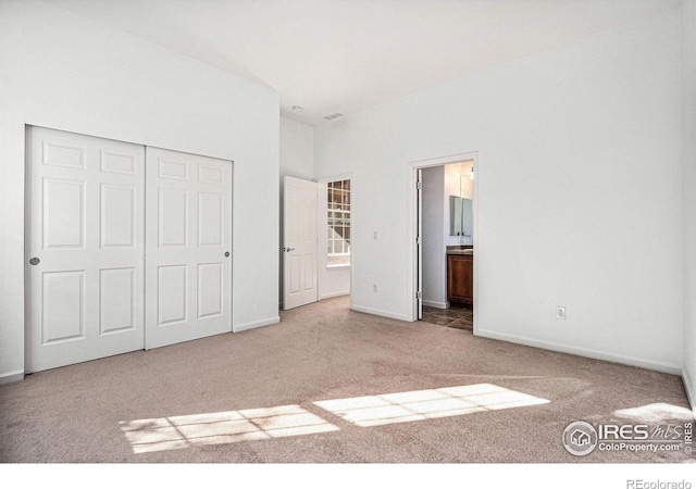 unfurnished bedroom with ensuite bath, a closet, and carpet flooring