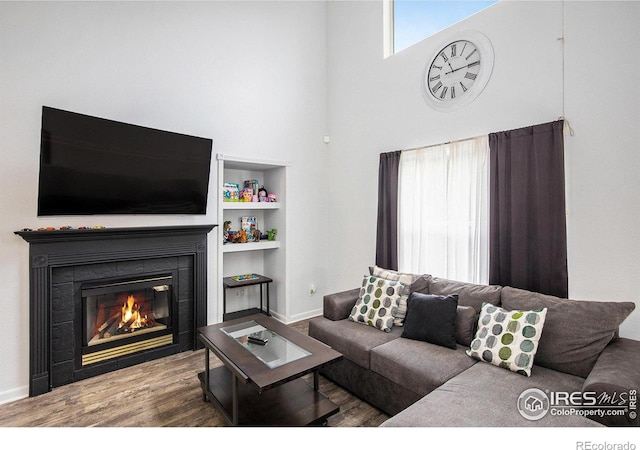 living room featuring a towering ceiling, hardwood / wood-style flooring, a fireplace, and built in features