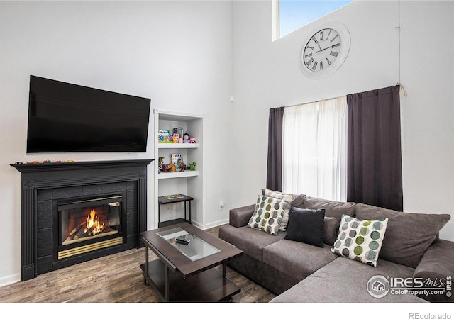 living area with baseboards, wood finished floors, a tile fireplace, and a towering ceiling