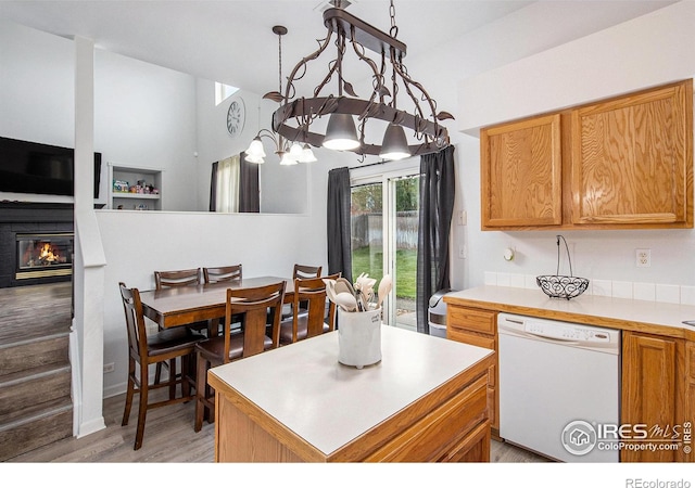 kitchen with light wood-style flooring, dishwasher, light countertops, and a glass covered fireplace