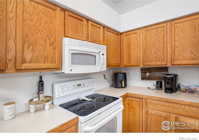 kitchen featuring backsplash, brown cabinets, light countertops, and white appliances