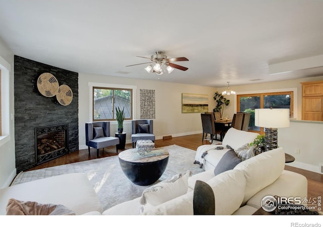 living room featuring ceiling fan with notable chandelier, hardwood / wood-style flooring, and a large fireplace