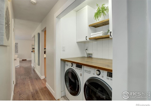 washroom featuring washing machine and clothes dryer, cabinets, and light hardwood / wood-style flooring