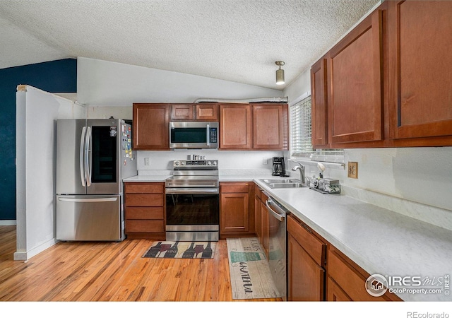 1900 Logan St, Longmont, CO 80501 - kitchen featuring a sink, stainless steel appliances, brown cabinets, vaulted ceiling, and light wood finished floors