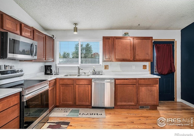 kitchen featuring light hardwood / wood-style floors, appliances with stainless steel finishes, sink, and a textured ceiling