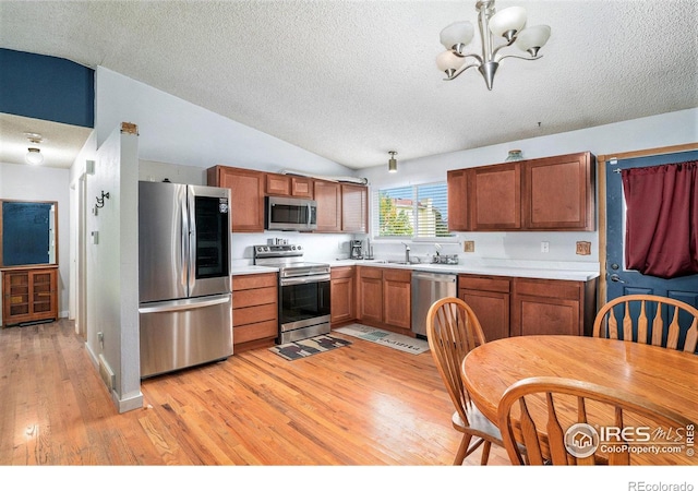 kitchen featuring pendant lighting, light hardwood / wood-style flooring, a chandelier, stainless steel appliances, and vaulted ceiling