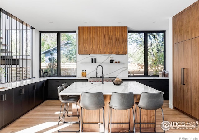 kitchen featuring light stone counters, expansive windows, an island with sink, a breakfast bar, and light wood-type flooring