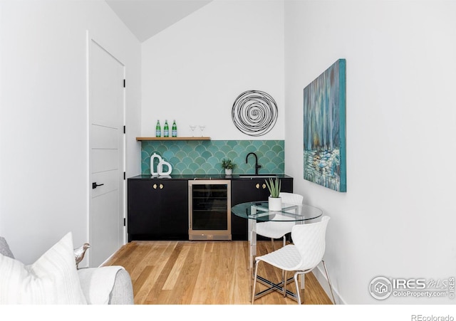 bar featuring lofted ceiling, sink, beverage cooler, backsplash, and hardwood / wood-style floors