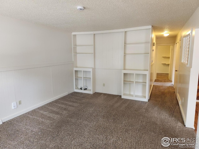 unfurnished bedroom featuring dark colored carpet, wooden walls, a closet, and a textured ceiling