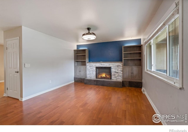 unfurnished living room featuring hardwood / wood-style flooring and a stone fireplace