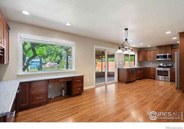 kitchen with pendant lighting, a wealth of natural light, stainless steel appliances, and light wood-type flooring