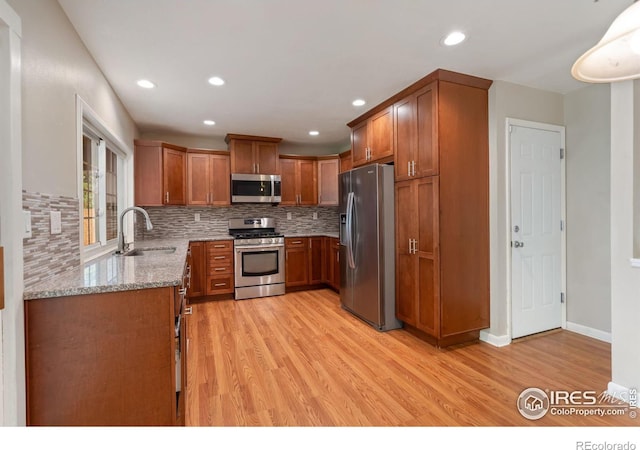 kitchen with sink, light hardwood / wood-style flooring, backsplash, appliances with stainless steel finishes, and light stone countertops